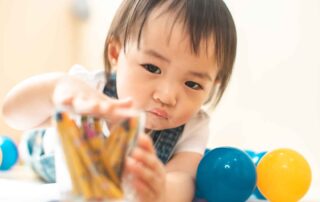 A young child focusing on fine motor skills development by handling small objects during an occupational therapy activity at OrbRom Center in Phnom Penh.