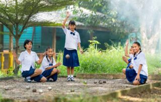 A group of young girls in school uniforms happily play petanque outdoors, showcasing teamwork, coordination, and communication