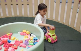 A young girl in Phnom Penh stacking colorful blocks on a toy car, engaging in a play-based occupational therapy activity to improve executive functioning skills.