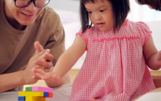 Young girl with Down syndrome playing with colorful blocks during an occupational therapy session with her parents, building motor and life skills.