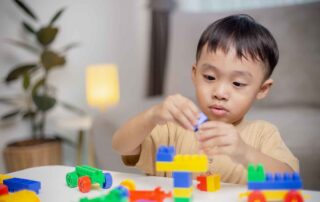 Child developing fine motor skills and problem-solving abilities through building activities during occupational therapy at OrbRom Center Phnom Penh