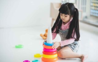 A young child practicing visual-motor integration skills by stacking colorful rings during an occupational therapy session at OrbRom Center in Phnom Penh.