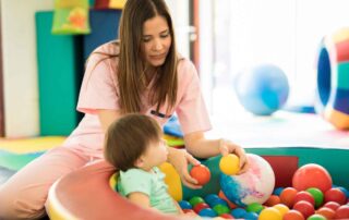 A therapist in Phnom Penh guides a toddler in a colorful ball pit during a sensory integration therapy session designed to support early development and coordination.