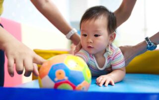 A young child practicing reaching and grasping skills with a colorful ball during occupational therapy at OrbRom Center in Phnom Penh.