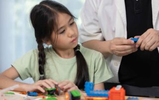 Child engaged in STEM-based learning while observing adult demonstration during an occupational therapy session in Phnom Penh