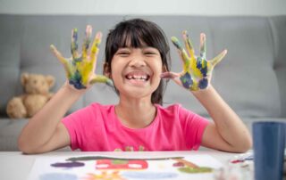 Smiling girl with colorful painted hands engaging in art activity that supports fine motor skill development during occupational therapy in Phnom Penh