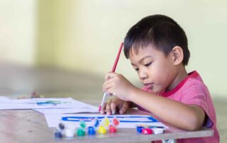 Young child engaging in fine motor skill development through painting activities during occupational therapy session at OrbRom Center Phnom Penh