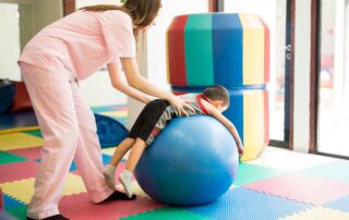 Occupational therapist assisting a child with therapy ball activities to build core strength and balance during an occupational therapy session at OrbRom Center Phnom Penh