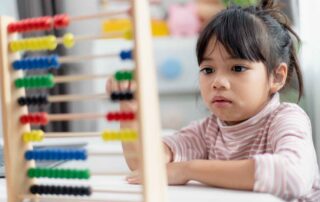 A young girl focuses on using a colorful wooden abacus, building fine motor skills and number concepts through occupational therapy activities.