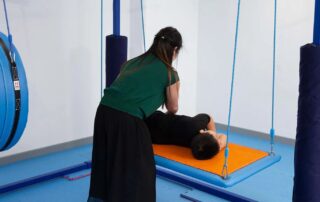 A therapist in Phnom Penh supports a child during sensory integration therapy on a suspended swing to improve balance and body awareness.