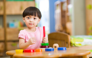 A young child participating in a fine motor activity with colorful stackable toys during occupational therapy at OrbRom Center in Phnom Penh.