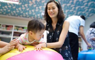 A therapist in Phnom Penh supporting a child with autism during a sensory-based occupational therapy session using a large therapy ball.
