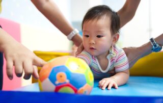 A baby engaged in a therapy activity with a colorful ball, supported by therapists—highlighting occupational and physical therapy techniques in Phnom Penh.