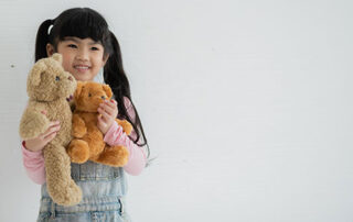 A smiling child in Phnom Penh holding teddy bears during occupational therapy, demonstrating emotional development through pretend play.