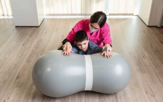 A therapist guiding a child through calming sensory input using a peanut ball during an occupational therapy session in Phnom Penh.