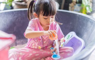 Child engaged in focused sand sensory play using scoops and containers during an occupational therapy session in Phnom Penh.