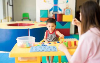 A young boy in Phnom Penh participating in structured play therapy with colorful sorting tools and peg boards, guided by a therapist to enhance motor and cognitive skills.