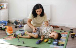 A therapist in Phnom Penh supports a young child with cerebral palsy during a play-based occupational therapy session using toy cars and gentle movement activities.