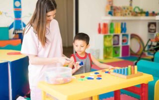 A therapist in Phnom Penh guiding a young child in a literacy-based occupational therapy activity using colorful alphabet pieces and sorting tools.