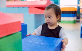 Young child building strength and coordination by lifting large blocks during occupational therapy session at OrbRom Center Phnom Penh