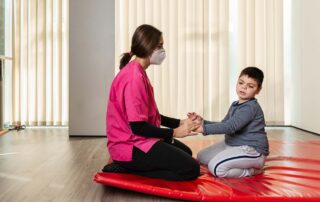 A therapist and young boy engage in an occupational therapy session on a red mat, focusing on motor coordination in Phnom Penh.
