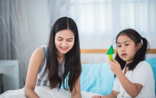 A young girl focuses on a green geometric toy as she engages in a skill-building activity with a supportive adult during a play-based therapy session.
