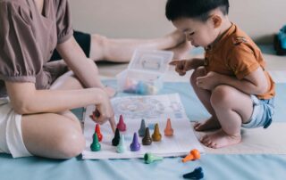 A toddler engages in a play-based therapy activity using colorful toys with an adult guiding cognitive and sensory development.