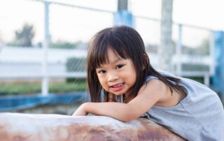 A smiling girl leans on a play structure during an outdoor occupational therapy session in Phnom Penh.