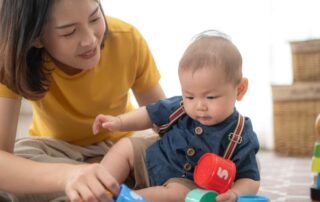 An infant plays with colorful cups while engaging in early developmental activities with a caregiver during occupational therapy in Phnom Penh.