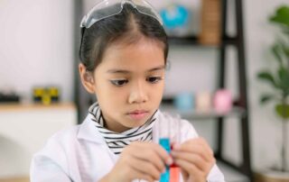 A focused child wearing safety goggles explores colored liquids in test tubes during an occupational therapy activity designed to build executive functioning.