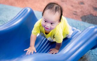 Toddler crawling up a blue slide during outdoor occupational therapy play session at OrbRom Center in Phnom Penh.