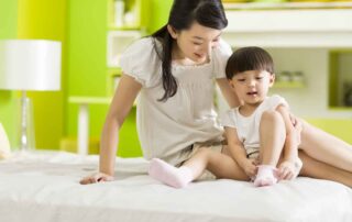 Child learning to put on socks with help from a caregiver, practicing self-care and independence at home in Phnom Penh.