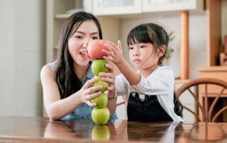 A child and therapist stacking apples together, engaging in a fun activity designed to improve motor planning, coordination, and focus at OrbRom Center in Phnom Penh.