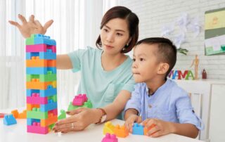 A child and therapist stacking colorful blocks together during a play-based occupational therapy session at OrbRom Center in Phnom Penh, developing motor and cognitive skills.