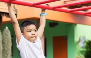 Young child building upper body strength on playground equipment during occupational therapy session at OrbRom Center in Phnom Penh.