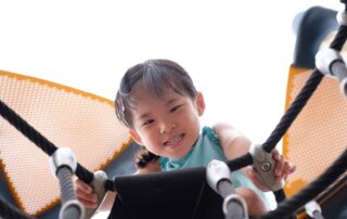 Smiling young child developing gross motor skills through climbing during occupational therapy session at OrbRom Center in Phnom Penh.