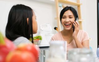 A mother smiling while on the phone and interacting with her daughter in the kitchen, modeling executive functioning during daily routines in Phnom Penh.