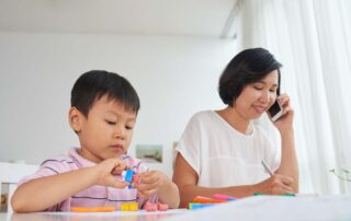 A young boy works with play dough while his mother takes notes, representing home-based activities that support occupational therapy.