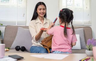 A young girl handing colored pens to her mother while preparing for a drawing activity, supporting fine motor development through occupational therapy in Phnom Penh.