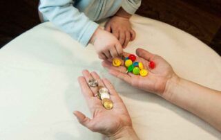 A child selecting colorful buttons and coins from adult hands as part of a fine motor skills activity during occupational therapy