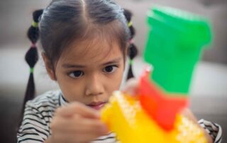 Young girl concentrating while building with colorful blocks during play-based occupational therapy session at OrbRom Center Phnom Penh