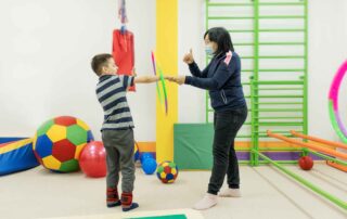 A therapist guiding a child through balance and coordination activities using colorful therapy tools in an occupational therapy room
