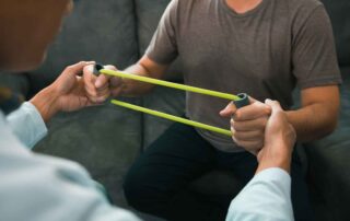 An adult using resistance bands during a supervised occupational therapy session focused on strength and motor control recovery in Phnom Penh