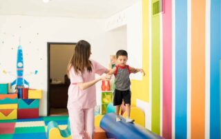 A therapist helping a child walk across a balance beam during a coordination-focused occupational therapy session in Phnom Penh