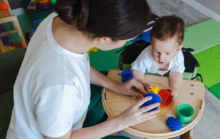 A therapist helping a baby develop fine motor and sensory skills using colorful stacking cups during an early intervention session in Phnom Penh