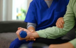 A therapist supporting a stroke patient using a hand weight during a strength-building occupational therapy session