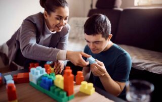 A therapist supporting a teen with Down Syndrome in a hands-on therapy activity using building blocks during an occupational therapy session