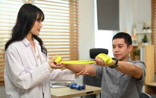 A young therapist assisting a teenage boy with resistance band exercises during an occupational therapy session in Phnom Penh