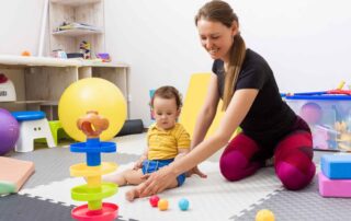 A therapist guiding a toddler through play-based activities using colorful balls and toys during occupational therapy in Phnom Penh