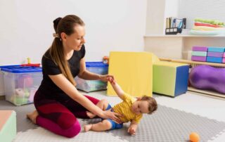 A therapist helping a toddler practice core strength and balance during a gross motor occupational therapy session in Phnom Penh